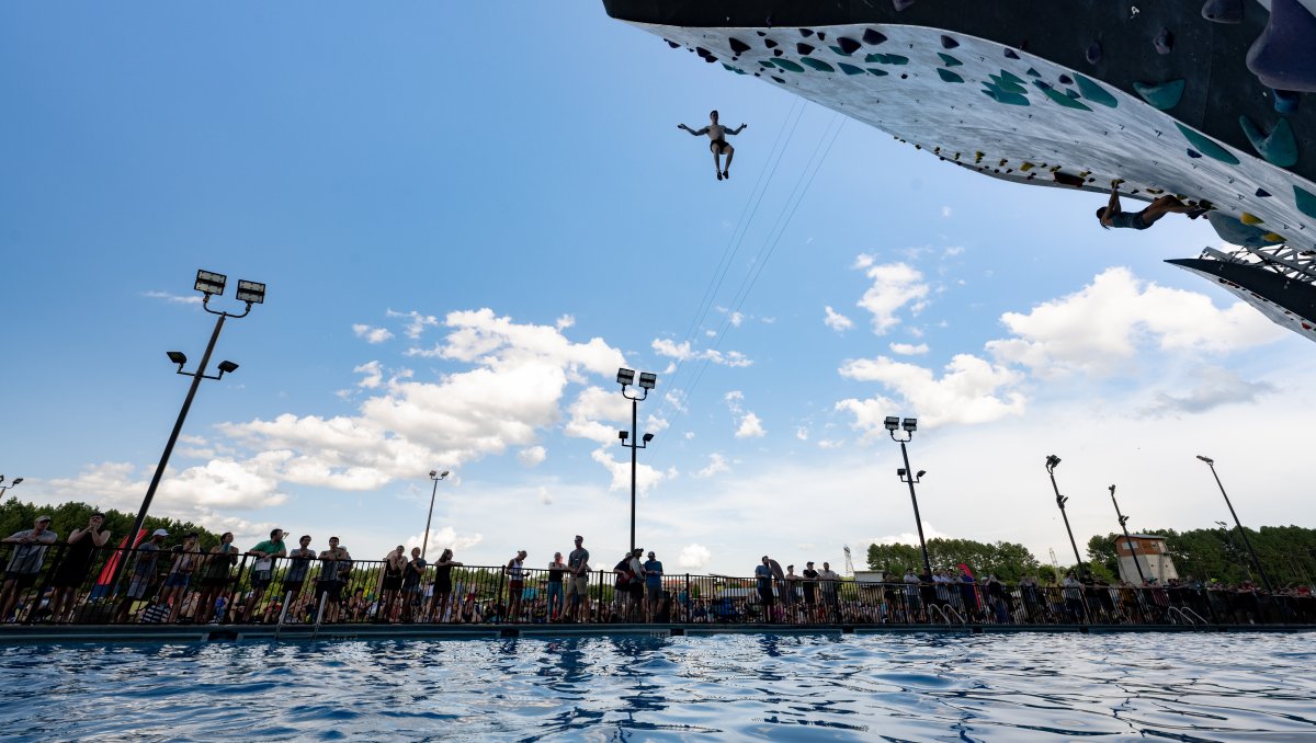 Person fall from top of rock climbing wall into water with spectators in background