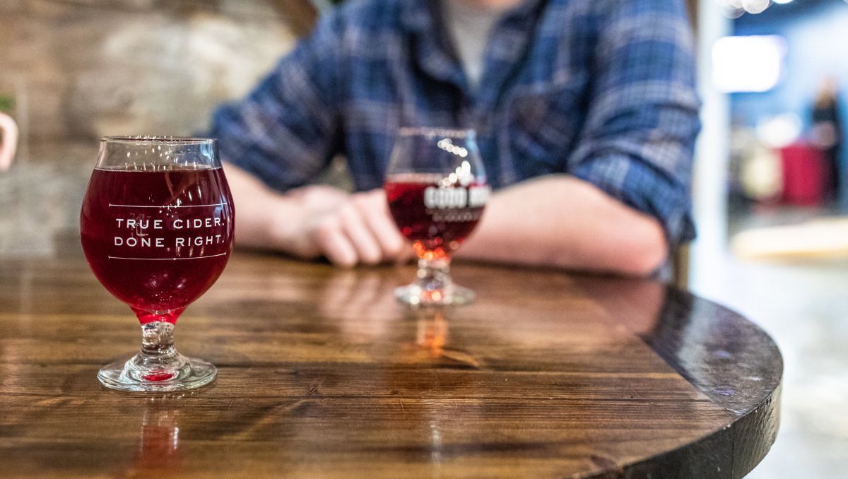 Two glasses of hard cider on table with man sitting at table