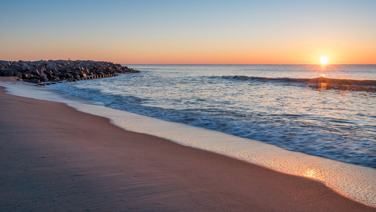 Sunrise to the left and rocks to the right with beach and water in middle at Fort Fisher State Recreation Area