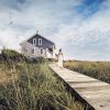 Woman walking on wood trail in marsh with rental house in background during daytime in Bald Head Island