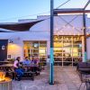 Friends sitting at table outside Neuse River Brewing Company in Raleigh at dusk with firepit and strung lights