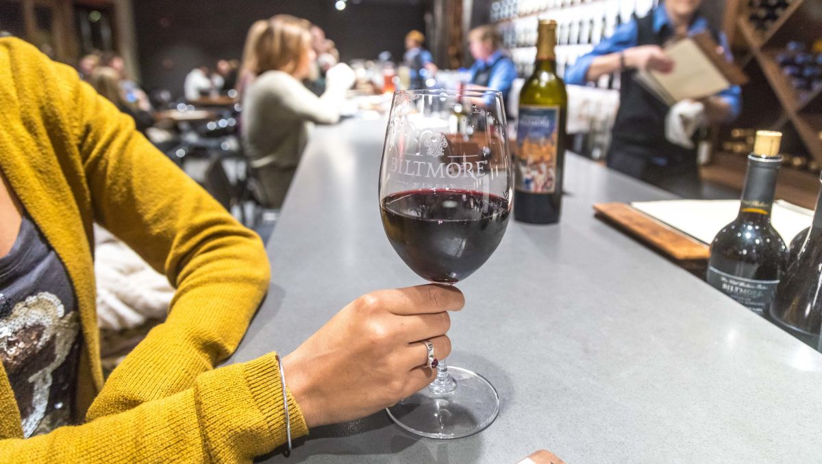 Woman in yellow sweater holding glass of red wine from Biltmore Winery on bar